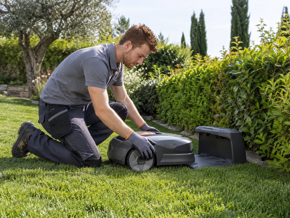 Tecnico accanto a un robot rasaerba e alla sua base durante un sopralluogo in giardino