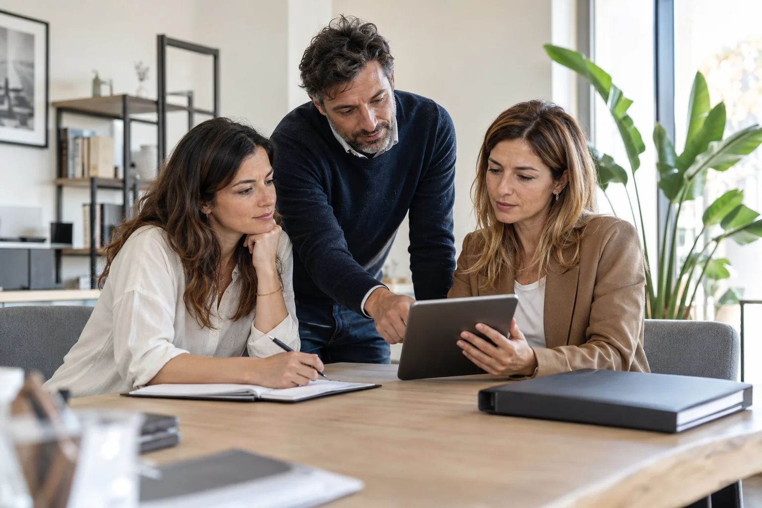 Tre professionisti consultano un tablet attorno a un tavolo nella sala riunioni luminosa di uno studio