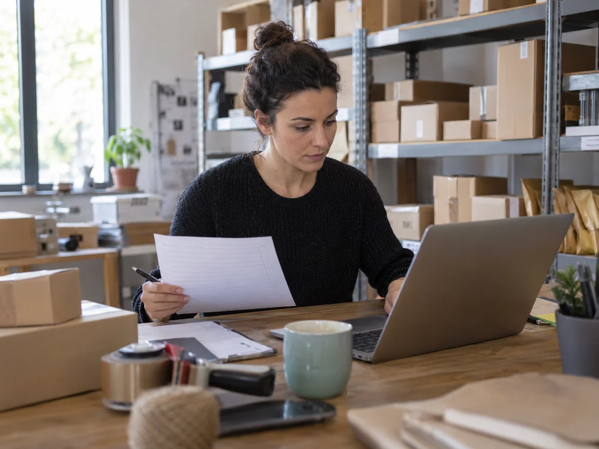 Una responsabile degli ordini controlla un portatile nel magazzino di un ecommerce, accanto a pacchi pronti per la spedizione